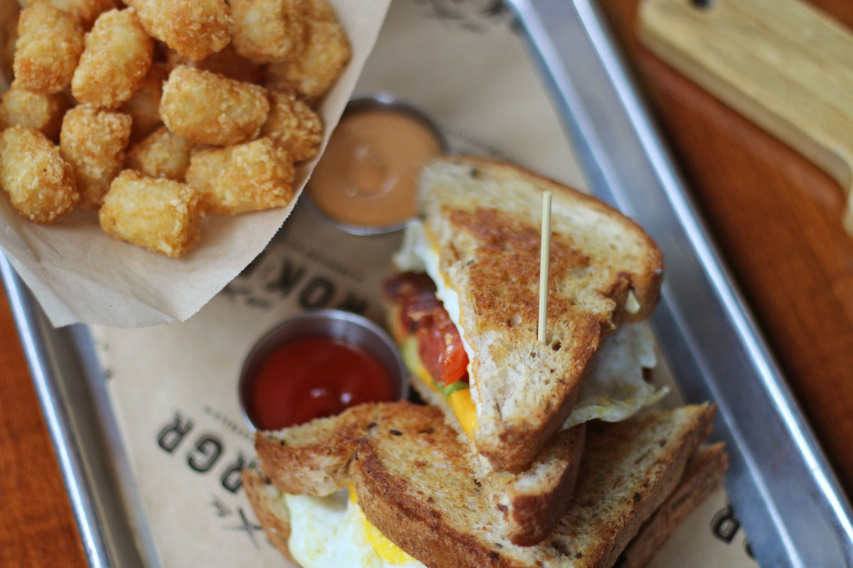 ROK:BRGR South Miami Saturday Brunch Hangover Sandwich with eggs, bacon, avocado, tomato, and cheese served with crispy tater tots